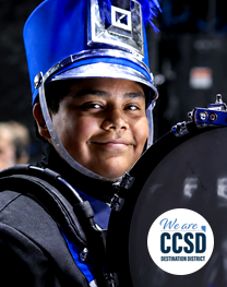 Portrait of a student wearing a blue-and-black marching band uniform and holding a percussion instrument during a band performance event.
