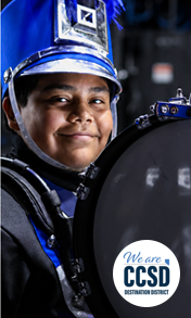 Portrait of a student wearing a blue-and-black marching band uniform and holding a percussion instrument during a band performance event.