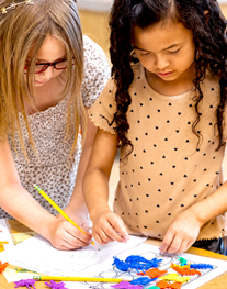 Two students working together on an art project, drawing and arranging colorful craft materials on a large sheet of paper.